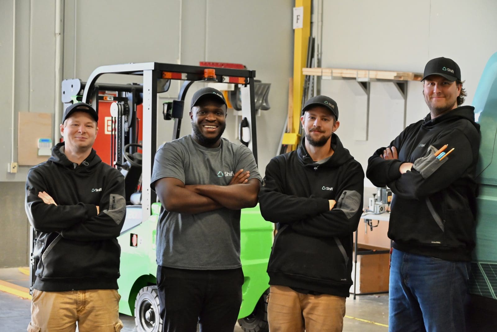 Four members of the Calgary installation team stand in a row inside the warehouse, smiling with their arms crossed
