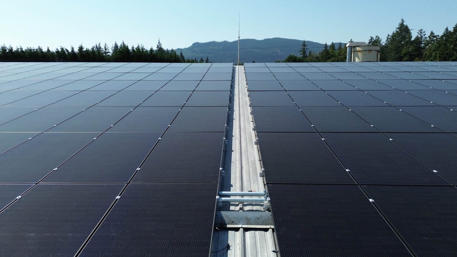 Rooftop view, looking down the middle of a large rooftop commercial solar panel installation.