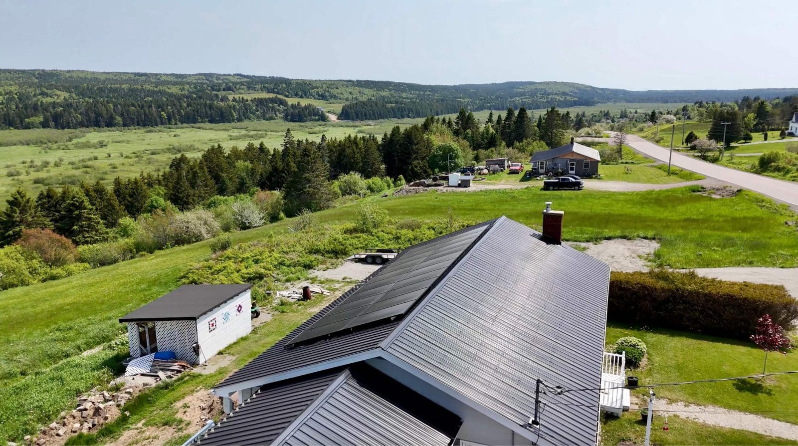 Aerial view of a rural home in New Brunswick. There is farmland, trees, and rolling hills in the background.