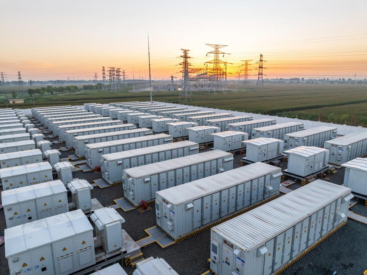 A utility-scale microgrid with battery storage in the foreground, and powerlines in the background.