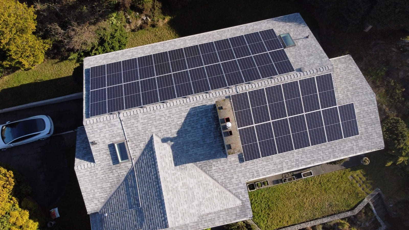 Aerial view of a home with solar panels on the roof and an EV in the driveway.