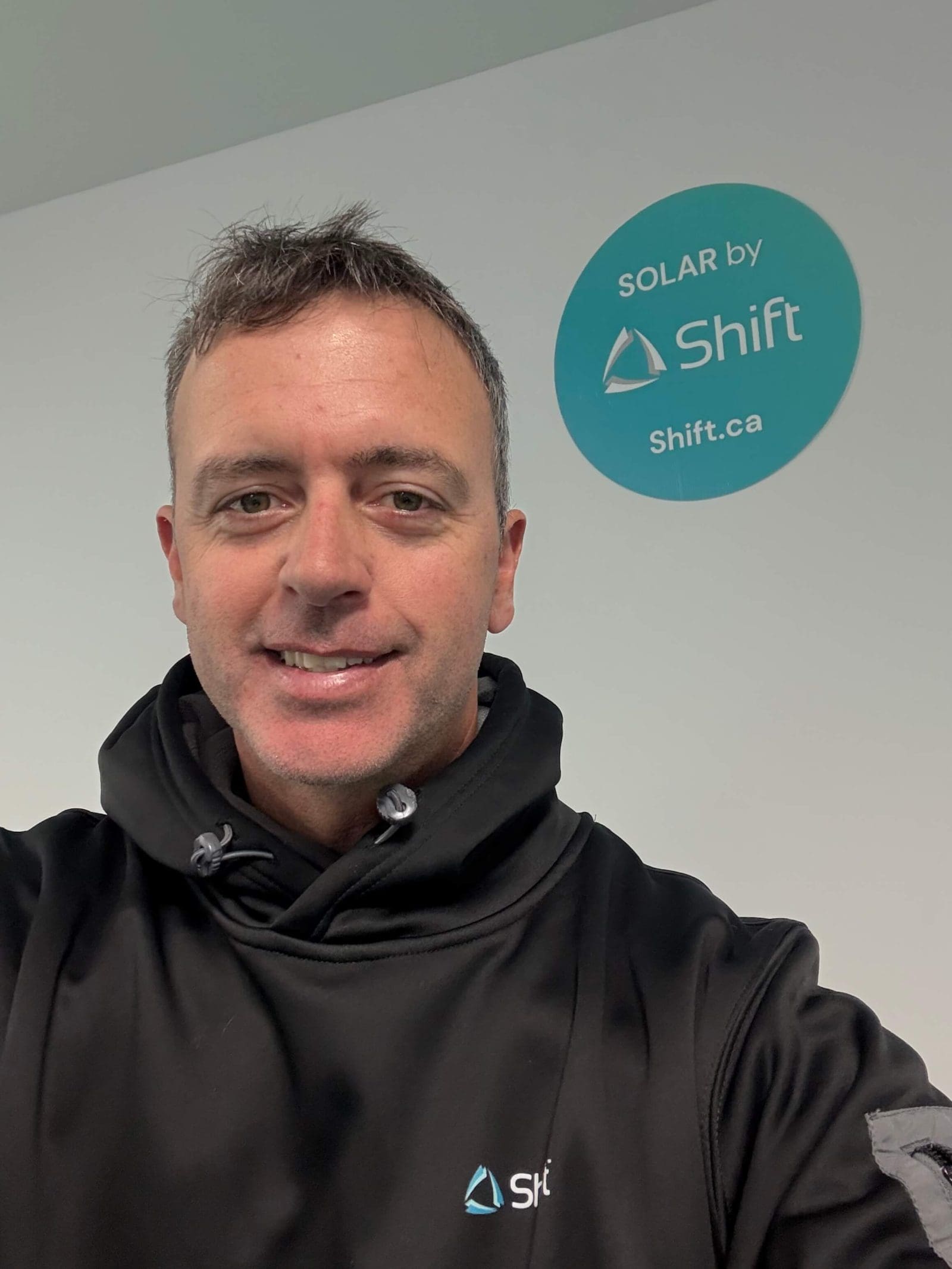 Selfie of a team member. There is a Shift sign on the wall behind them.